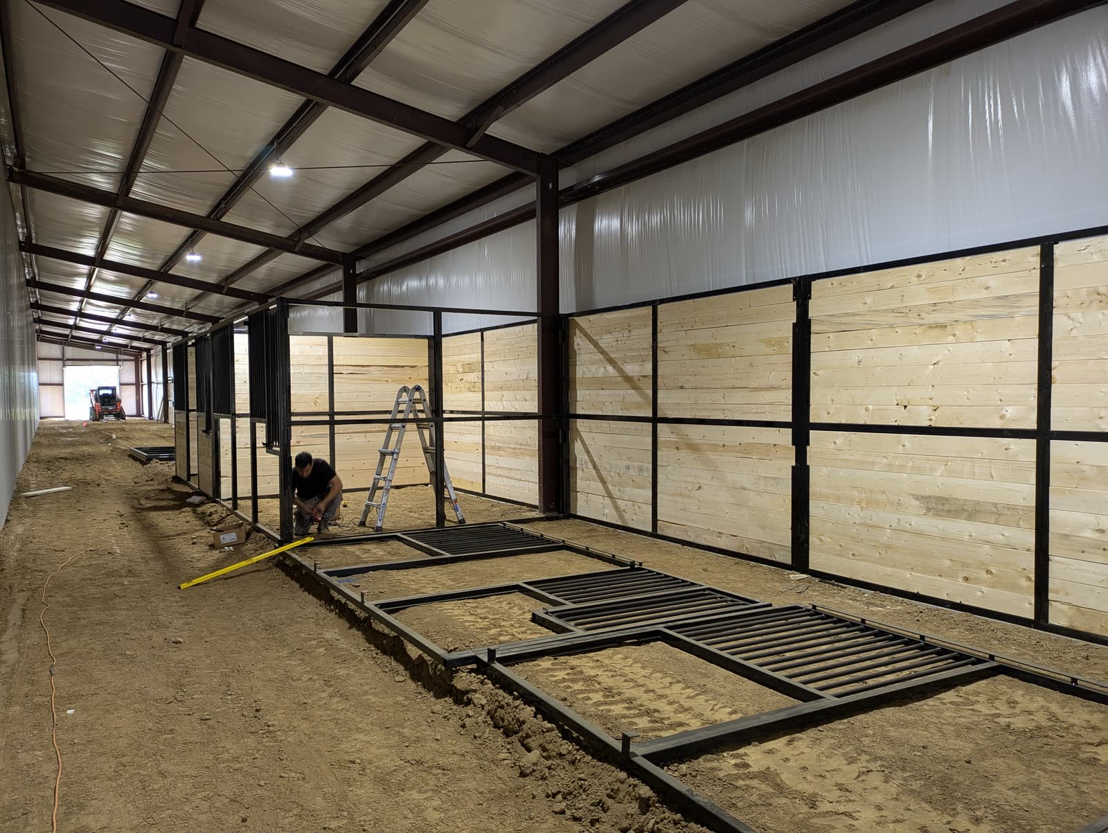 Crew member assembling stall frames on the floor beside standing wood-infill stall walls