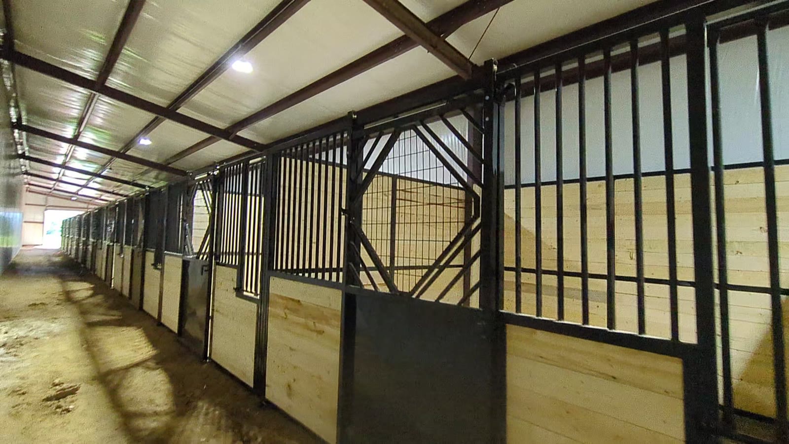 Aisle view of finished stall fronts with vertical bars, grille panels and black steel doors