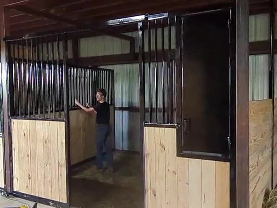 Video still: a person standing beside the barred divider with wood below, closed in place between the two new stalls