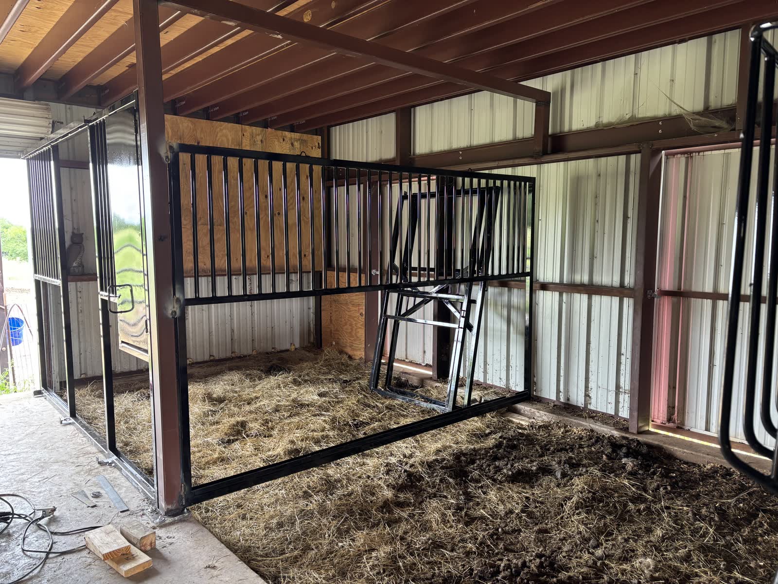 Install in progress: a black steel stall-front frame and a barred divider frame standing in the bedding