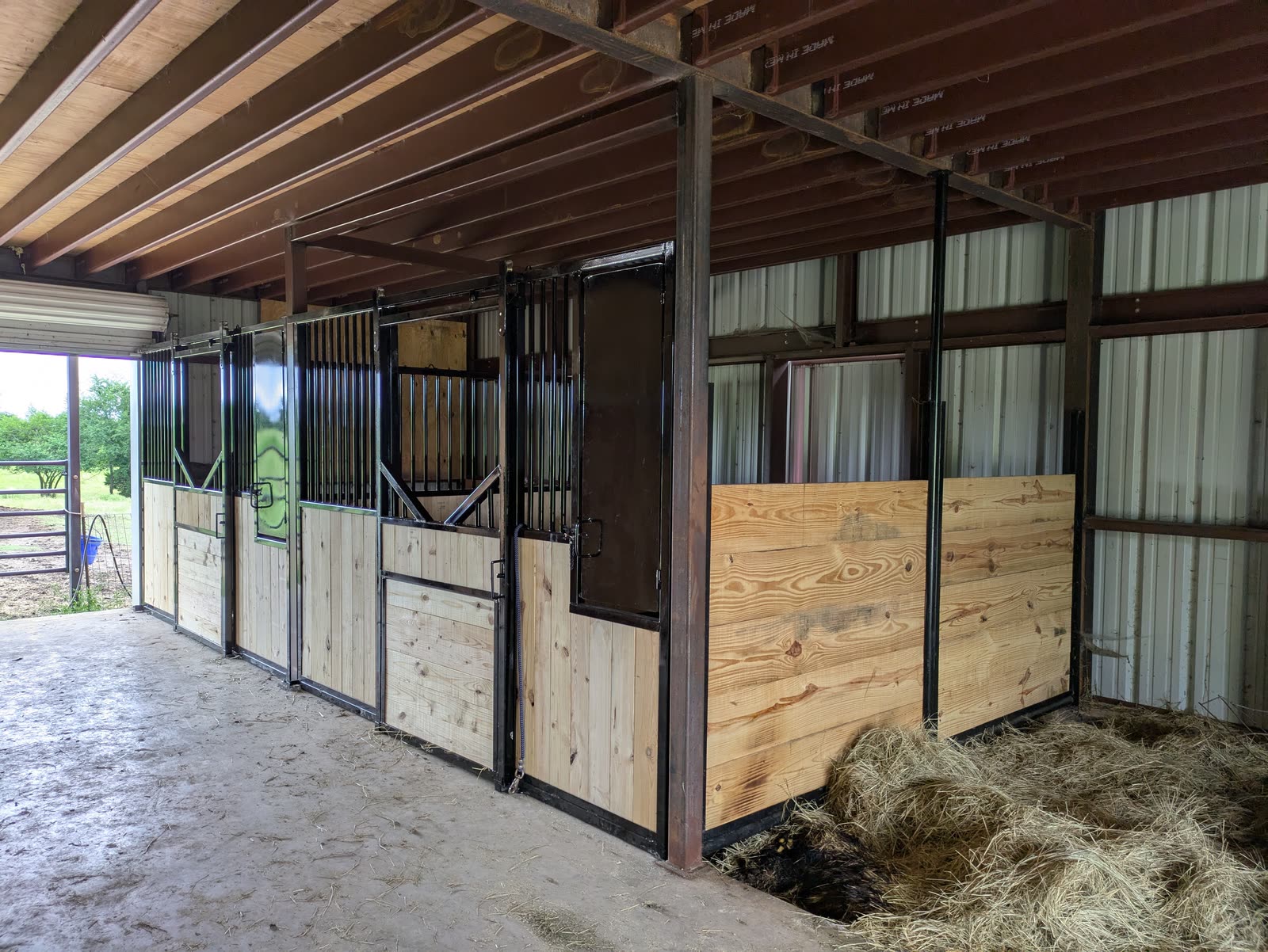 Two finished stalls in a steel building in the Sherman, Texas area: black steel fronts with vertical bars over pine boards, sliding doors, and a full-height pine end wall